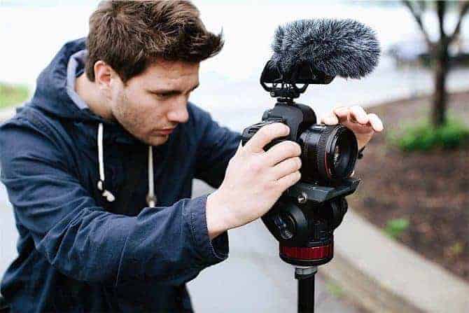 Man setting up camera with a shotgun microphone attached to top.