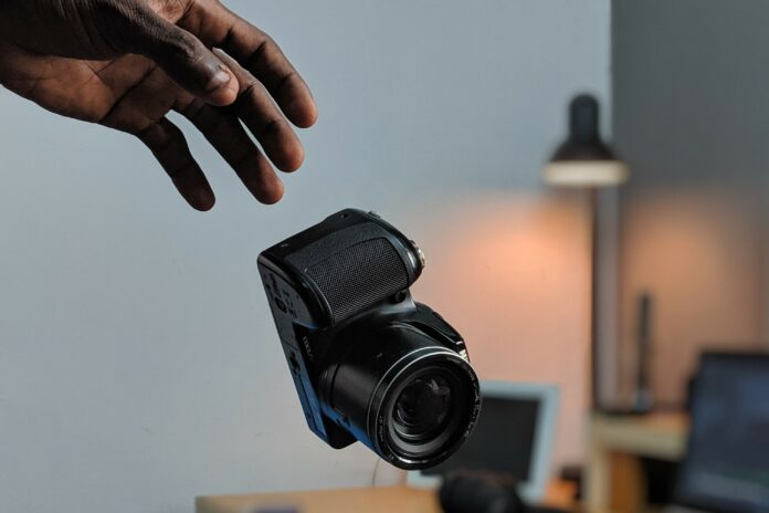 Hand reaching out toward a falling black Nikon COOLPIX bridge camera with a desk in the background.