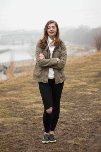 Woman in ripped black jeans and a jacket shivering near a misty pond