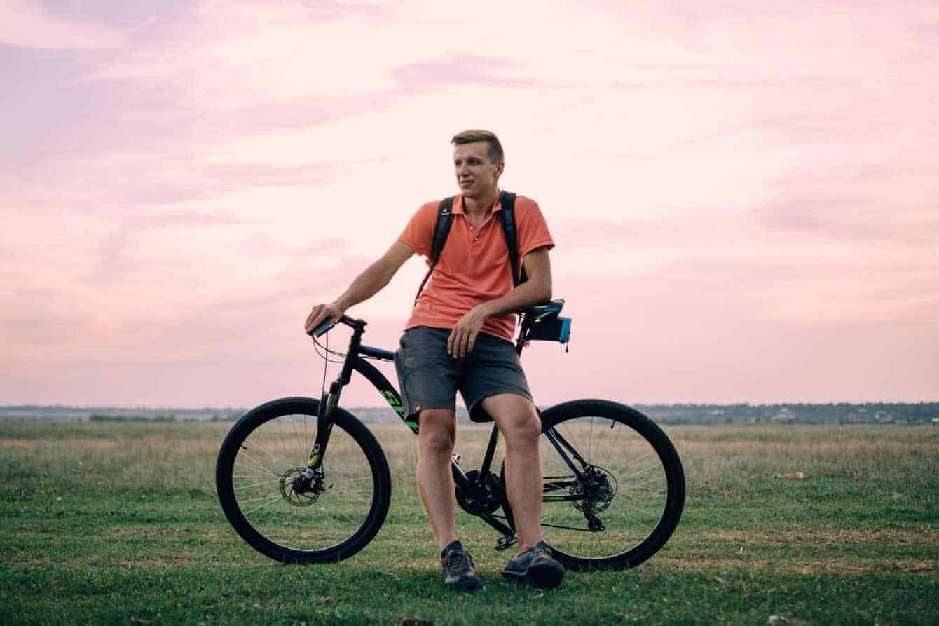 A full-body portrait of a cyclist in a vibrant sunset, showcasing the subject relaxed on a mountain bike against a grassy field, perfect for capturing dynamic outdoor.