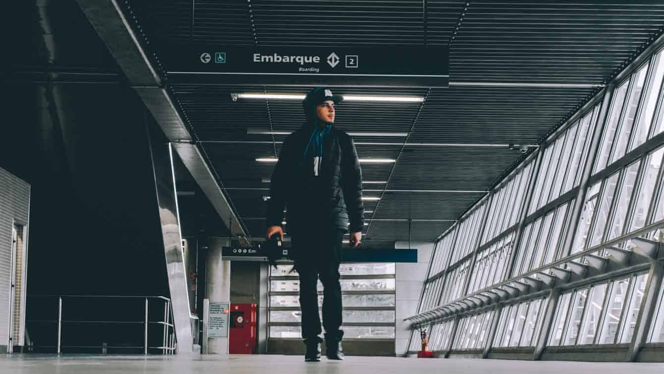 Person in dark clothing carrying a camera through an airport with a red door in the background