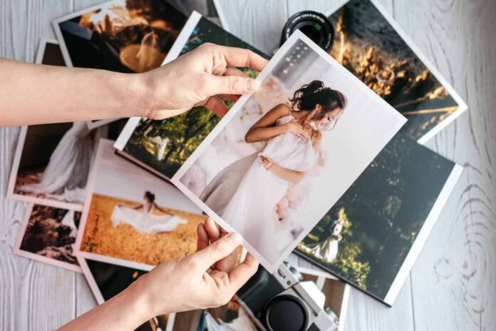 Hands holding photograph of woman in white dress above pile of photos on table.