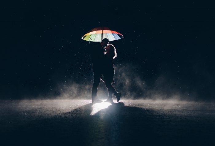A silhouette of a couple under an umbrella in the rain at night.