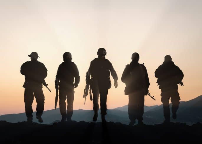 Military silhouettes of soldiers against the backdrop of sunset sky.