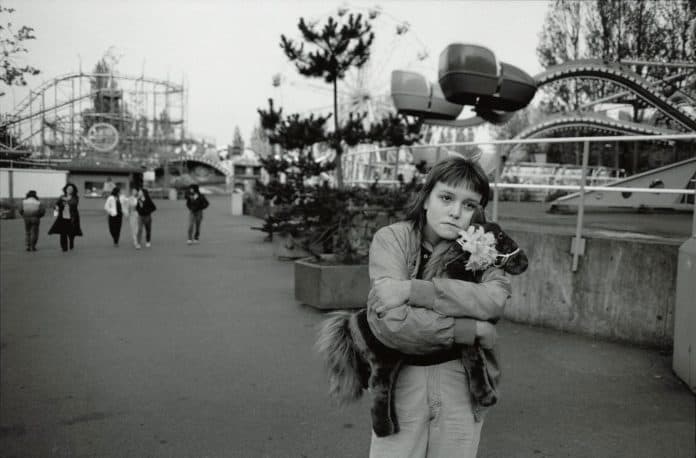A poignant black-and-white image featuring a girl holding a cat, set against a whimsical amusement park backdrop. It captures emotion and nostalgia, showcasing moments of.