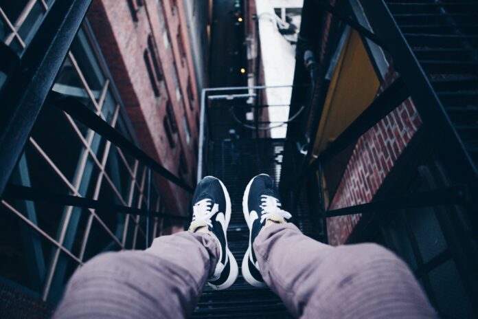 Perspective of a guy sitting on high fire escape looking down at his feet dangling between buildings.