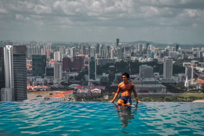 Dark haired, tanned model sitting on ledge of infinity pool at Marina Bay Sands, Singapore.