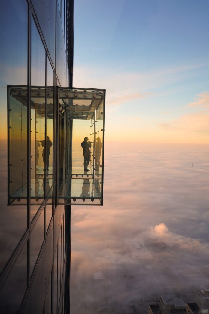 Silhouette of a man standing inside the glass box of the Ledge, Skydeck Chicago at Willis Tower, against sunset.