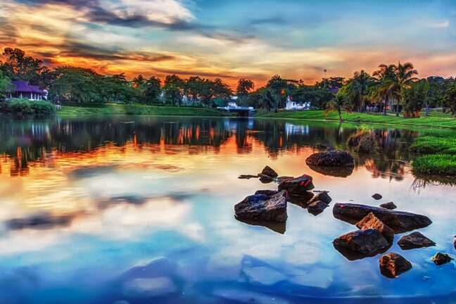 HDR edited landscape photo of small lake with trees and houses in background.