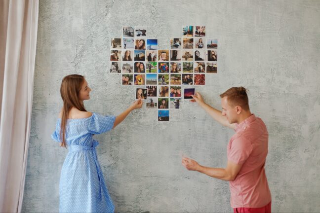 Man and woman creating a heart-shaped wall collage with photo prints.