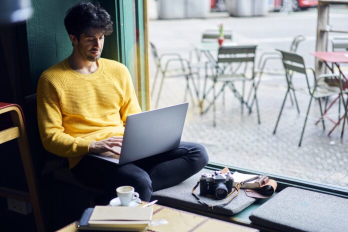 Man on laptop browsing online with camera in a coffee shop.
