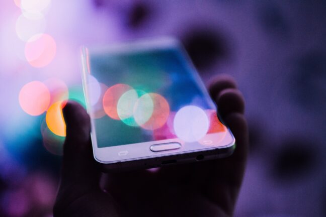 Hand holding a smartphone with lights in the background