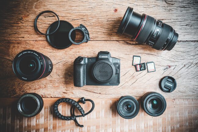 A camera, several lenses, memory cards, and several filters laid out on a wooden table