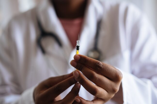 Doctor in white lab coat holding a needle with yellow liquid