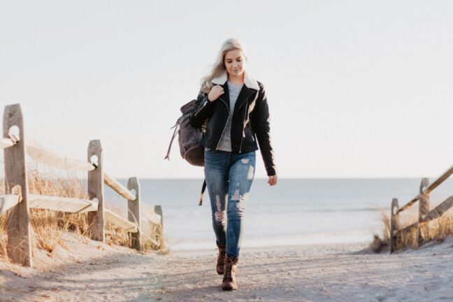 Young blonde woman walking up sandy path away from the beach