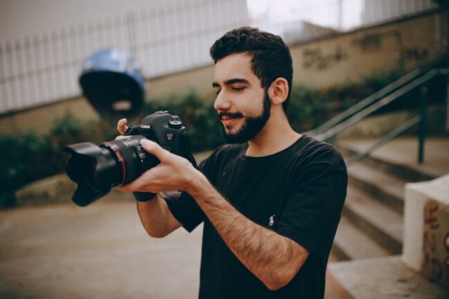 Dark-haired man with beard holding a camera in front of him looking at the LCD