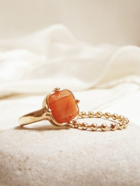 Gold ring with orange gemstone next to a gold bracelet on bedding.