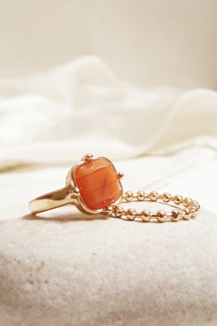 Gold ring with orange gemstone next to a gold bracelet on bedding.
