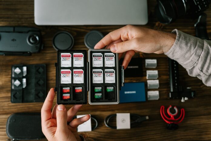 Man's hands holding an SD card case above a table filled with camera gear.