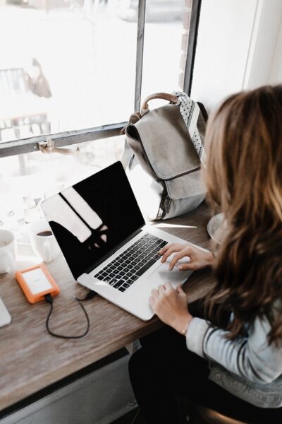 Woman using an orange LaCie external hard drive with a laptop while sitting by a window.