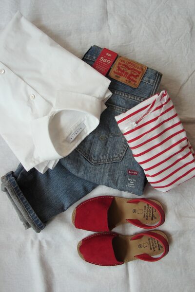 A red-striped top, red shoes, jeans, and a white shirt laid out on white sheets.