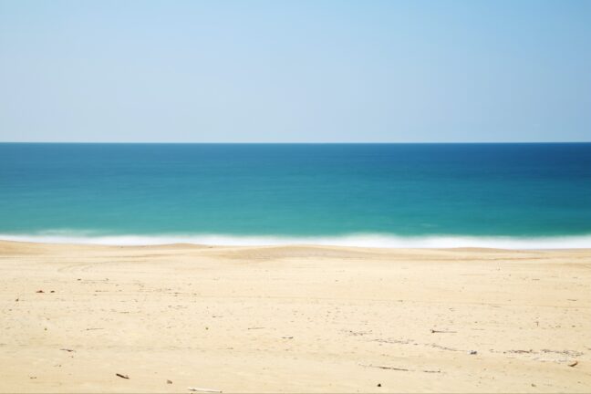 Yellowish sand beach with blurry waves and a turquoise ocean in the background.