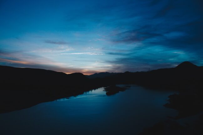 Blue sky after sunset with a dark lake in the foreground.