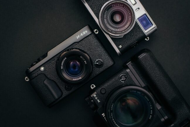 The Fujifilm X100S, the Fujifilm X-T2, and the Fujifilm X-E2S arranged geometrically on a black surface.