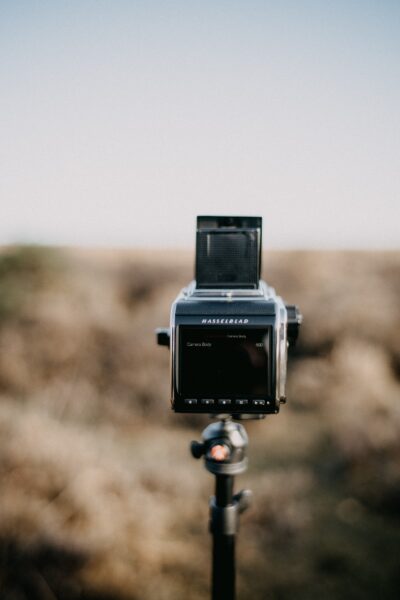 A boxy Hasselblad camera with a black LCD mounted on a tripod and a blurry field in the background.