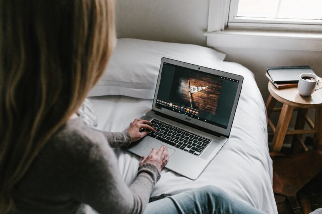 A woman with long hair sitting in front of a laptop on a bed while editing an image of a flag.