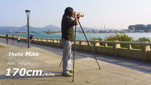 Person using the Theta Max tripod and a telephoto setup on a pathway by water with boats and buildings in the distance.