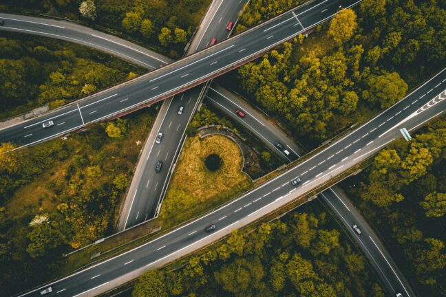 A busy highway intersection from above with green trees and tiny cars.