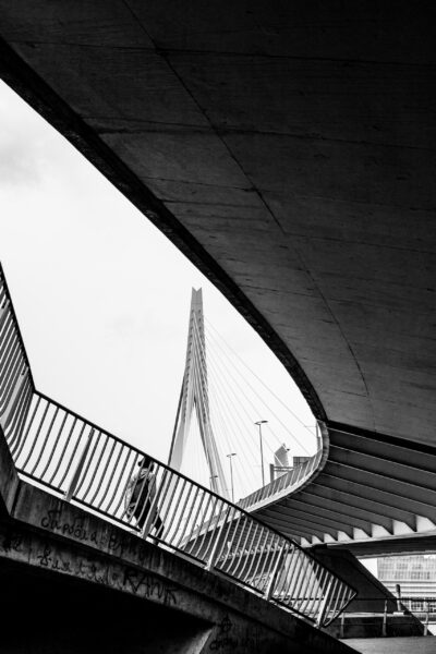 Concrete structures with a person walking move toward a bridge tower in the distance against a white sky.