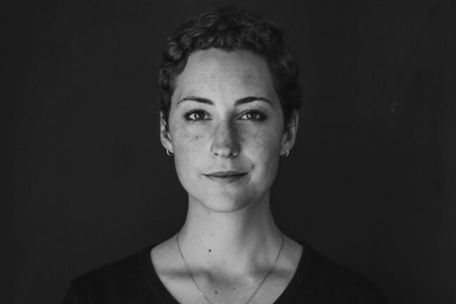 A B&W headshot of a woman with short hair and a slight smile standing against a dark background.