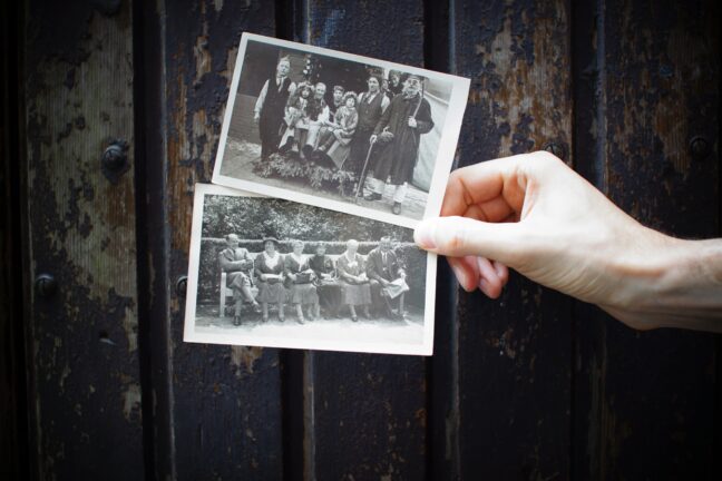 A hand holds out two black and white photo prints of people in front of a wood background.