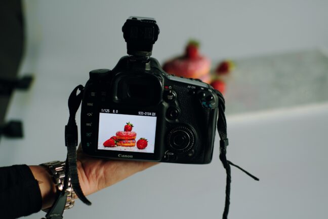 Hand holding a camera that shows a donut photo on the LCD with the actual arrangement in the background.