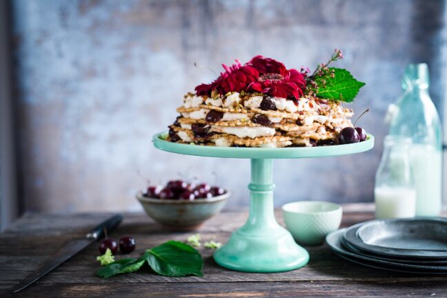 A raised platter with dessert and flowers on a wooden table surrounded by dishes.