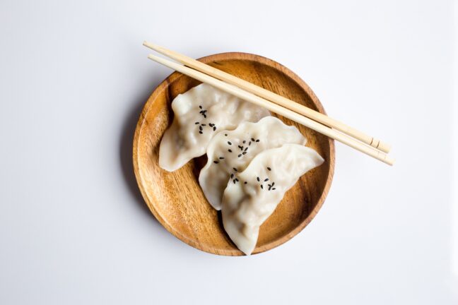 Three seasoned dumplings on a wooden plate with chopsticks.