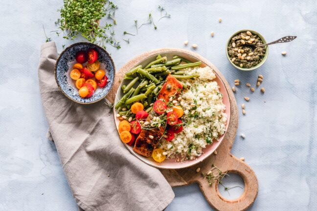 A meat, vegetable, and rice dish with pesto and tomato side dishes on a white cloth.