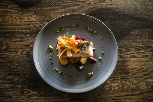 A small meal surrounded by drizzled pesto on a gray plate on a wooden table.