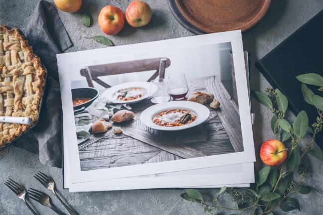 Printed photos of food on a table surrounded by apples and pies.