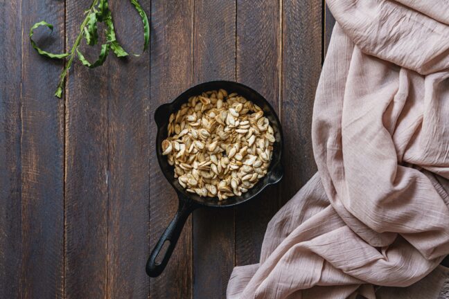 Pumpkin seeds in a black pot with white cloth on a wooden table.