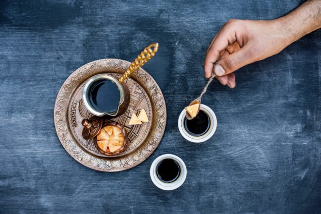 Hand tilting a piece of food into a cup of liquid over a dark textured surface.