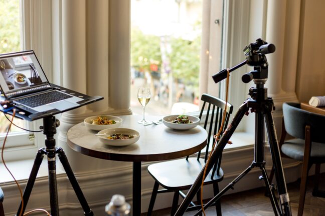 A tripod and a laptop positioned next to a table with three dishes and a glass.