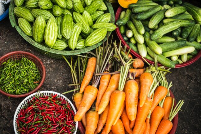 Carrots, cucumbers, and other vegetables arranged on a dark surface.