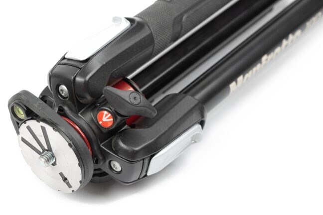 A black Manfrotto tripod without an attached head lying on a white surface.