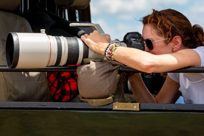 Female professional photographer on safari. Woman rests camera on a bean bag and shoots wildlife from a safari vehicle. in the Masai Mara, Kenya.