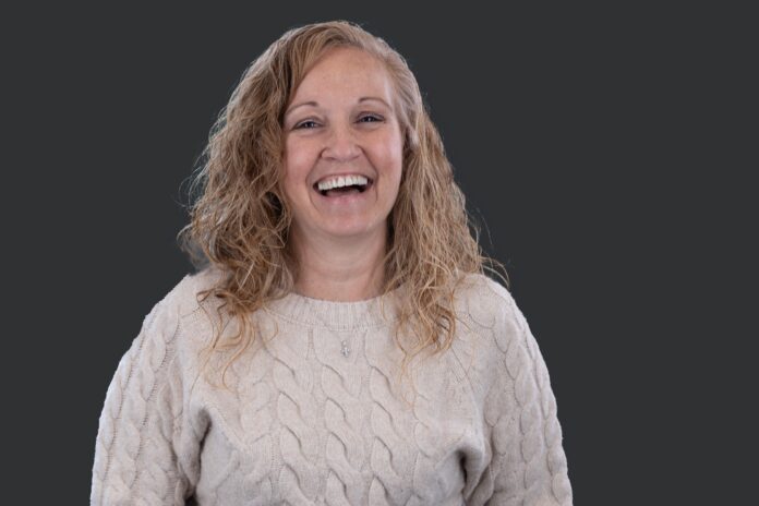 Headshot of woman with blond hair laughing against dark backdrop.