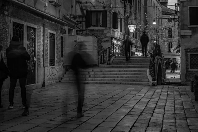 Venice street at night in black and white with motion blur of people walking.