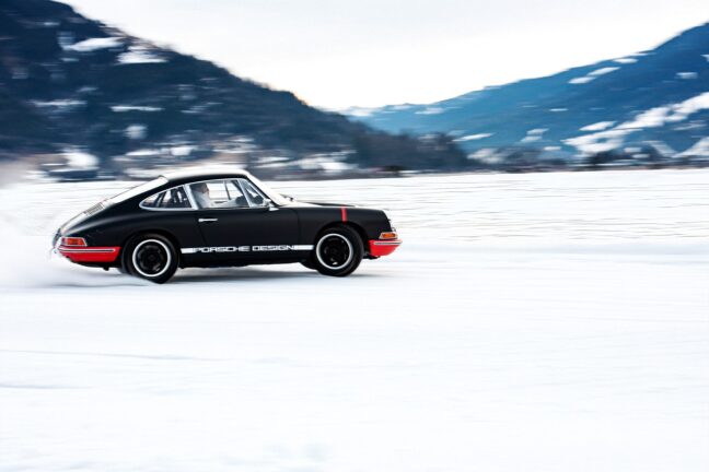 A black Porsche with "Porsche Design" written on the side is speeding across a snowy landscape with motion blur in the background, highlighting the car's movement.